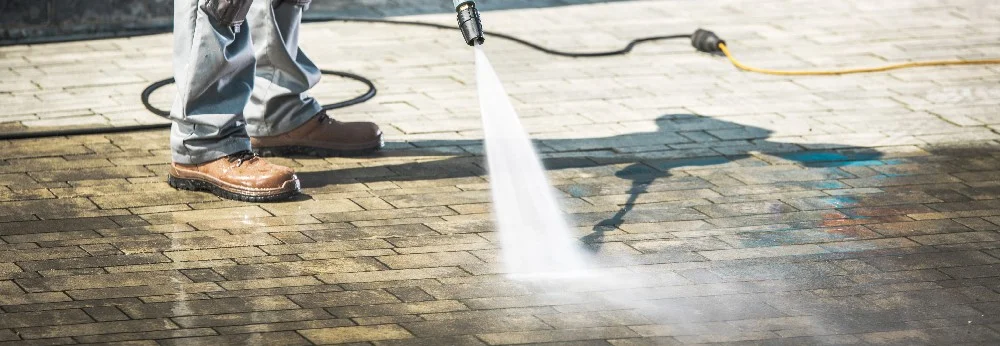 Person reinigt Pflaster mit Hochdruckreiniger